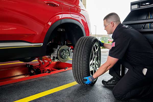 Certified Valvoline Instant Oil Change technician performing a tire rotation on a red vehicle