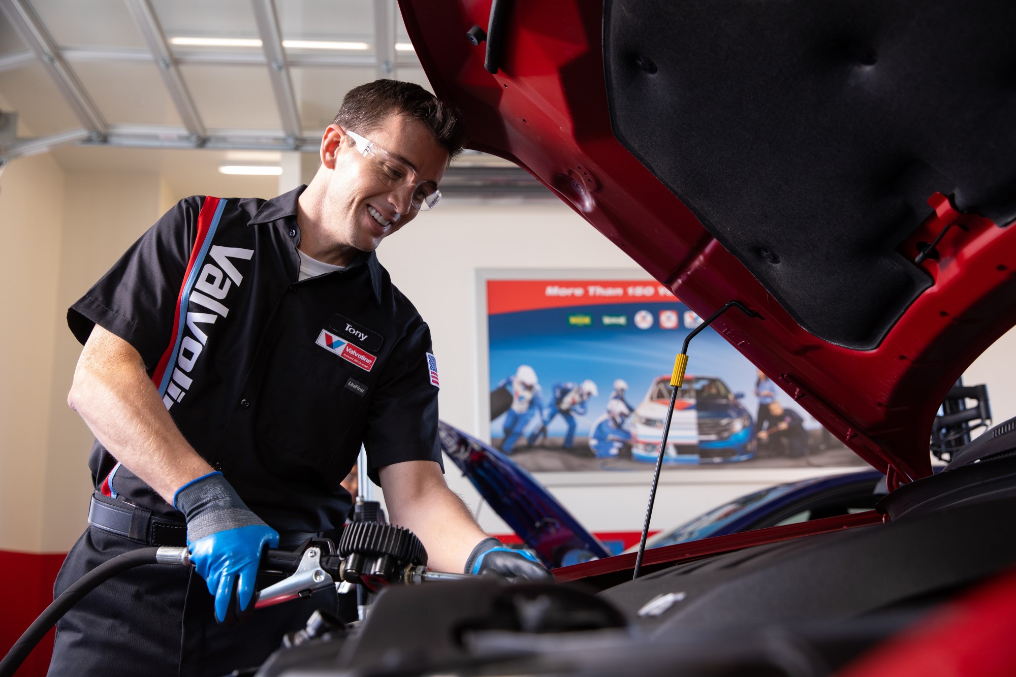 Certified Valvoline Instant Oil Change technician performing an oil change on a red vehicle