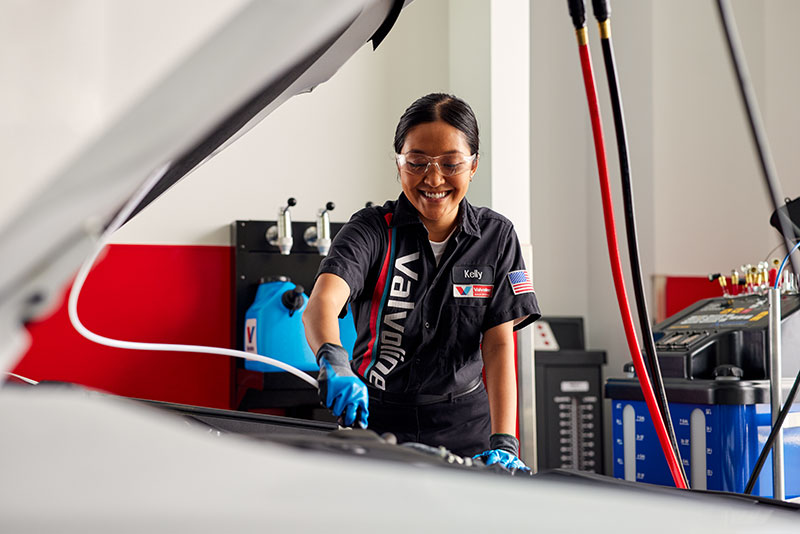 Certified Valvoline Instant Oil Change technician servicing a transmission under the hood of a grey vehicle