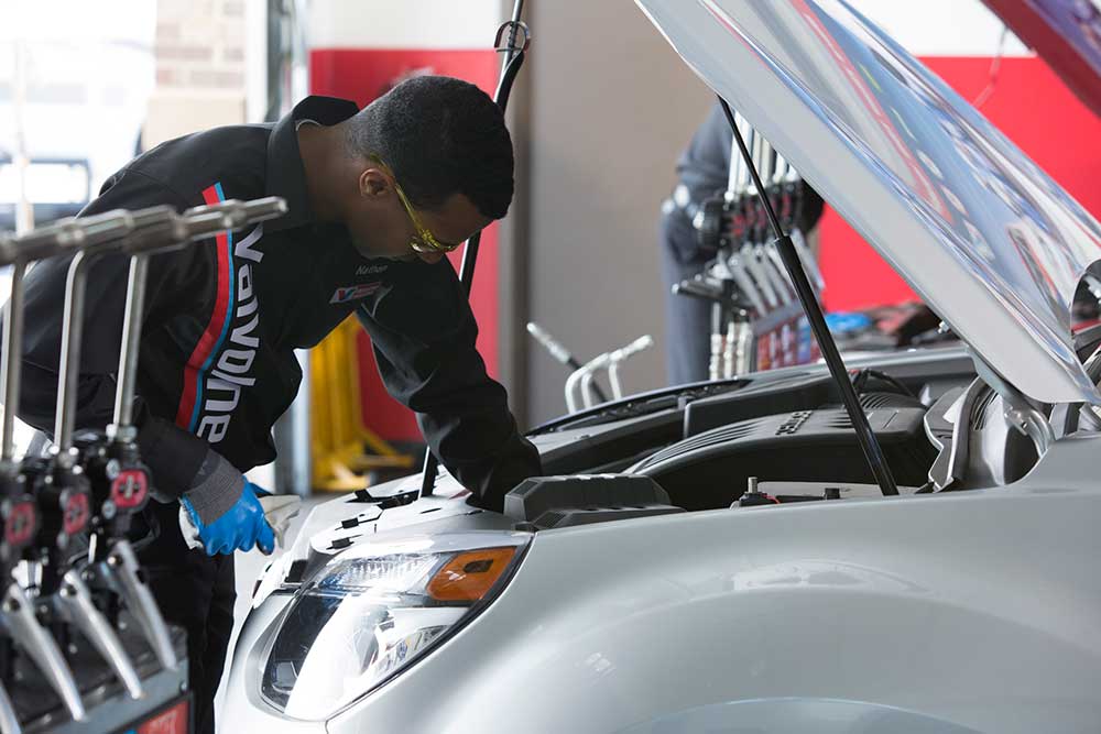 Certified Valvoline Instant Oil Change technician performing radiator maintenance on a grey vehicle