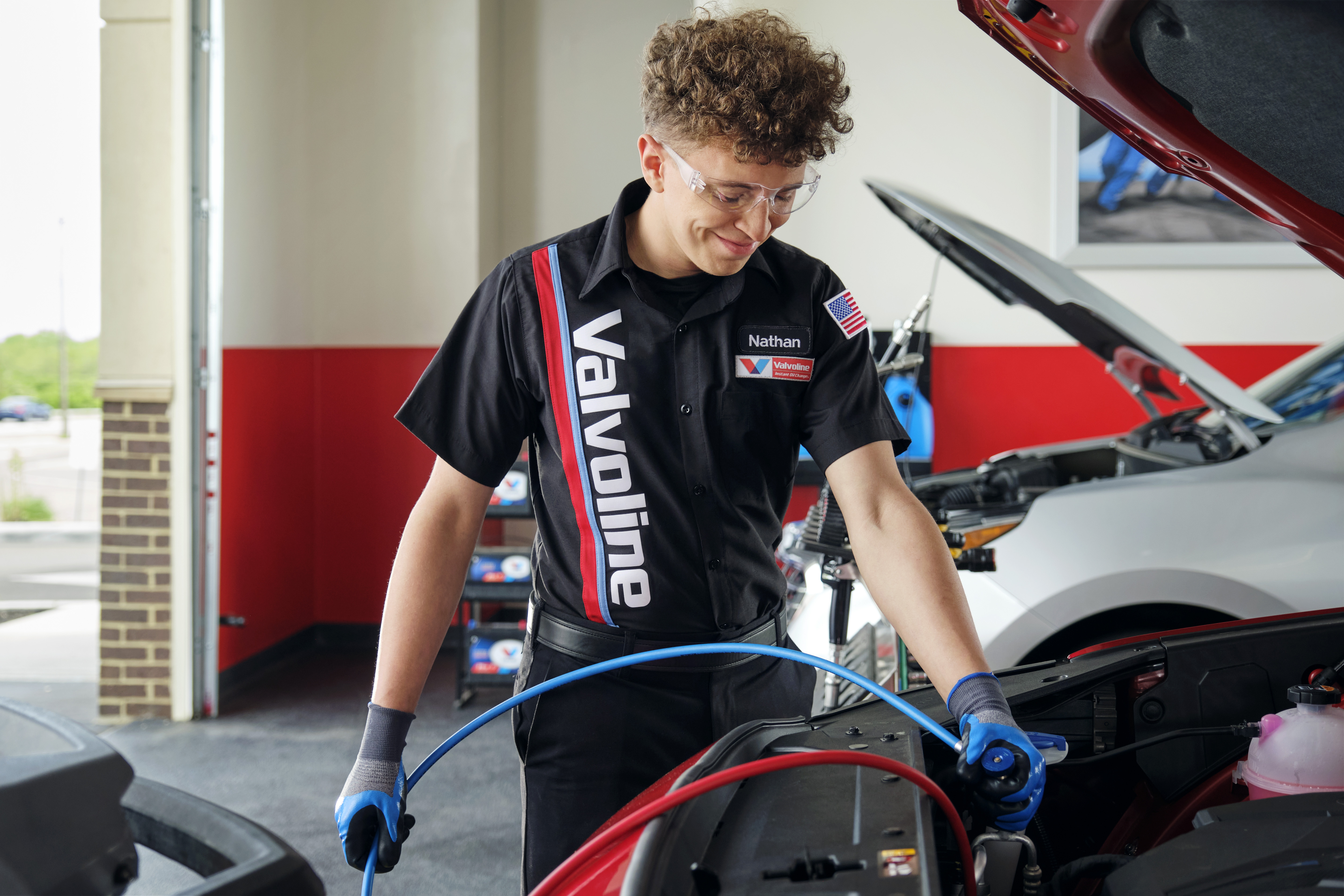 Certified Valvoline Instant Oil Change techician smiles as he recharges A/C on customer car