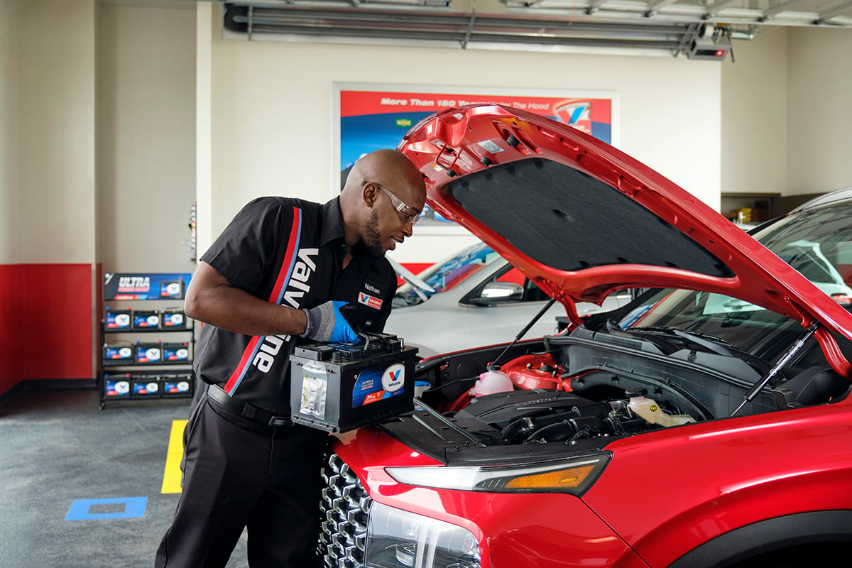 Valovline Instant Oil Change Certified Technician servicing a red vehicle and replacing the battery under the car hood