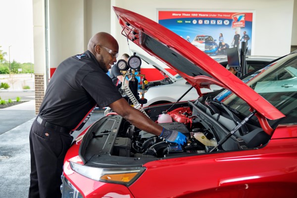 Certified Valvoline Instant Oil technician performing a service under the hood of a red vehicle